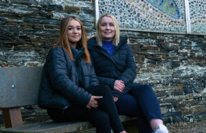 Image of a mentor and mentee posing for a photograph, sitting on a bench by a school.