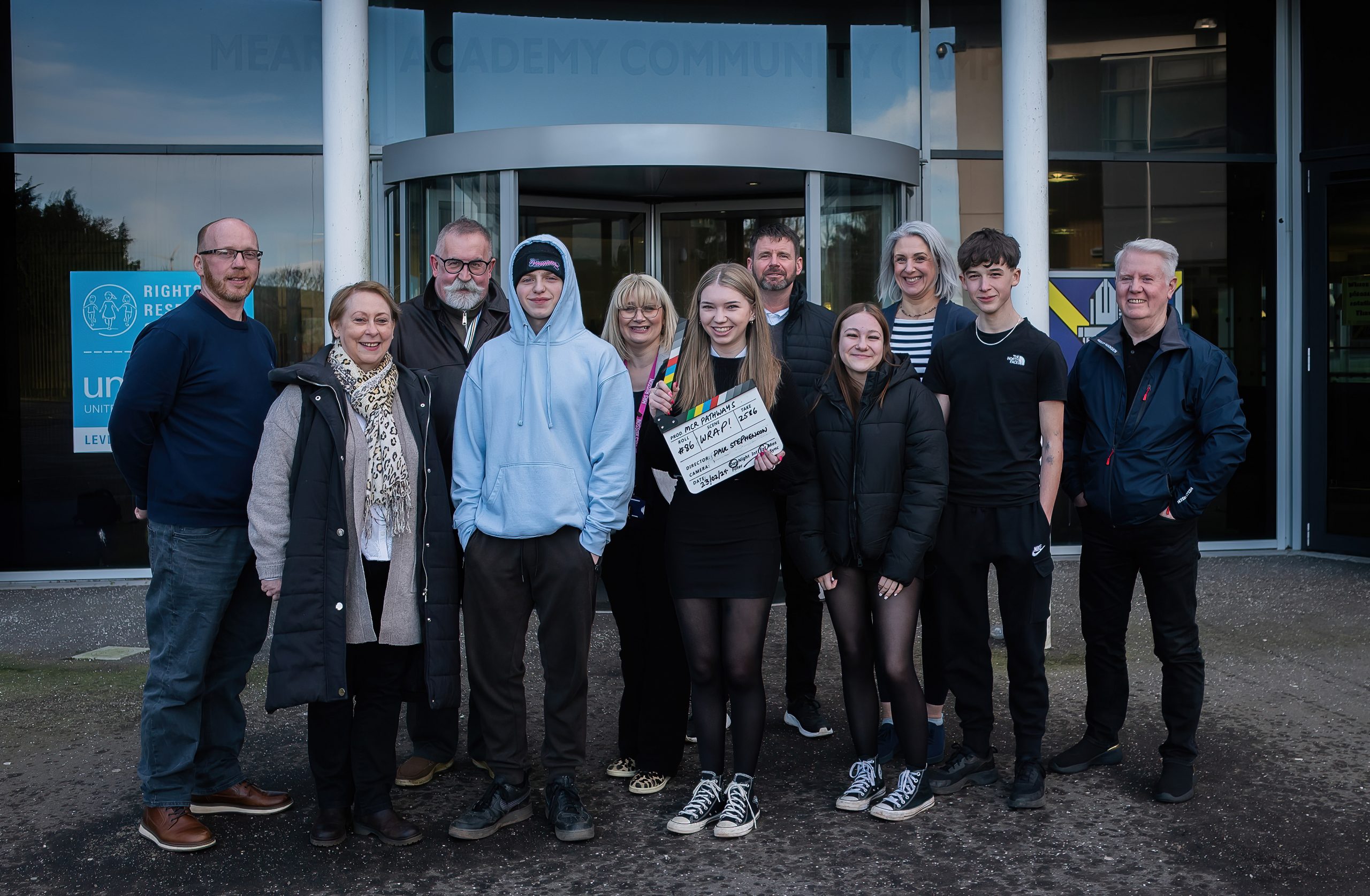A group of people standing together outside a building entrance, smiling for a group photo.